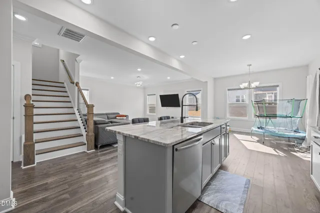 a kitchen with granite countertop a refrigerator oven a sink dishwasher and white cabinets with wooden floor