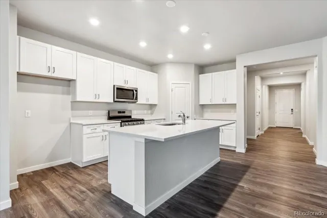 a kitchen with stainless steel appliances a stove top oven a sink a refrigerator white cabinets and wooden floor