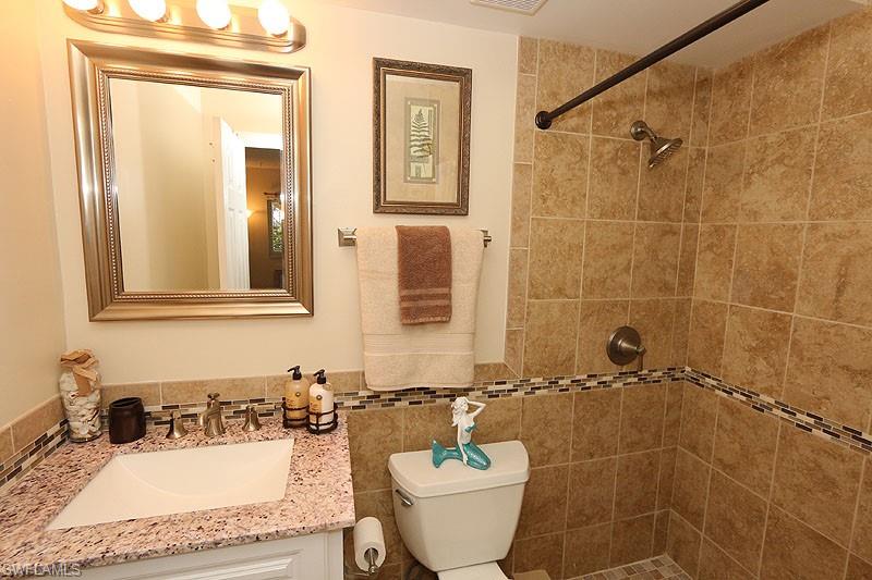 820 Ketch Drive, Unit 2 Naples, FL 34103 - Photo 11 of 17 Bathroom with tiled shower, tile walls, toilet, tasteful backsplash, and vanity