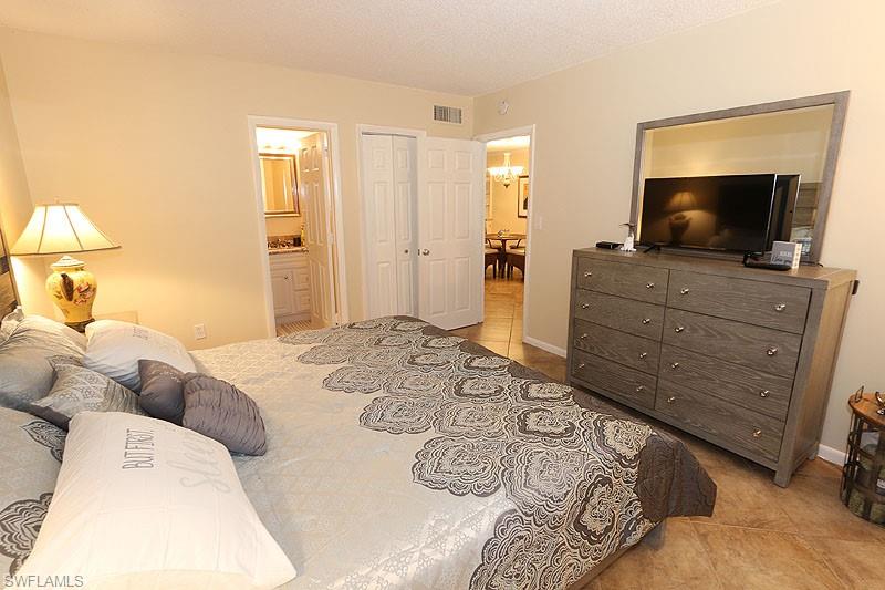 820 Ketch Drive, Unit 2 Naples, FL 34103 - Photo 10 of 17 Bedroom featuring a notable chandelier, a closet, ensuite bathroom, and light tile floors