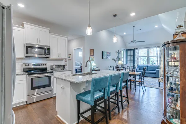 a kitchen with stainless steel appliances granite countertop a stove a sink a microwave a dining table and chairs with wooden floor