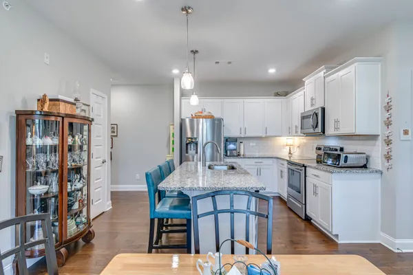 a kitchen with stainless steel appliances granite countertop a dining table chairs refrigerator and cabinets