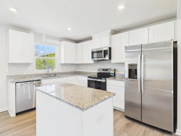 a kitchen with kitchen island granite countertop a refrigerator a sink a stove a microwave and island with wooden floor