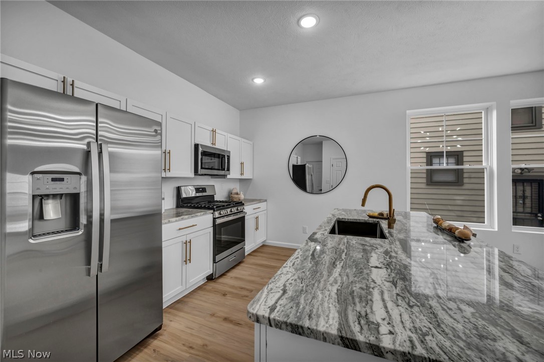 3633 Pennington Road Cleveland, OH 44120 - Photo 11 of 34 Kitchen featuring stainless steel appliances, light stone counters, white cabinets, light wood-style flooring, and an island with sink