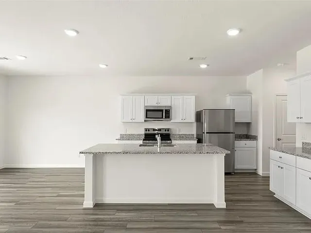 a view of a kitchen with stainless steel appliances granite countertop a stove top oven a sink and white cabinets
