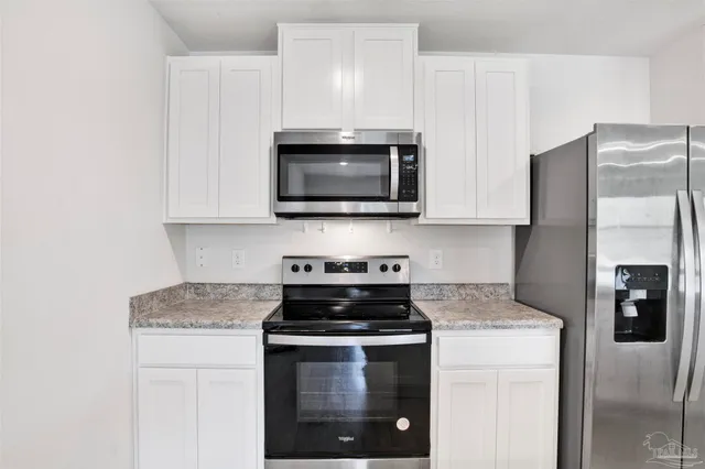 a kitchen with stainless steel appliances granite countertop white cabinets a stove a microwave and a refrigerator