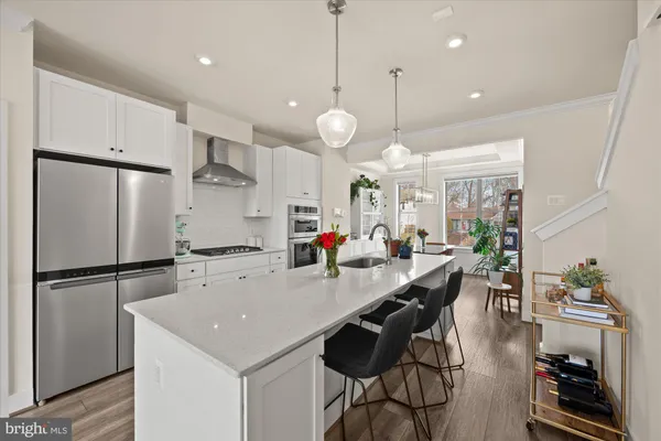 a kitchen with stainless steel appliances a stove a refrigerator a sink a dining table and chairs with wooden floor