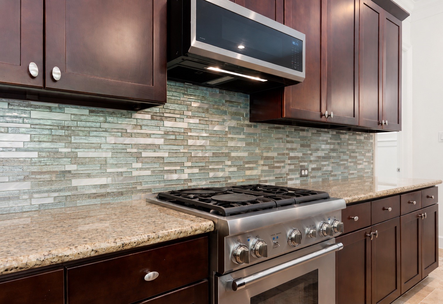 1904 Boulder Ridge Drive Conroe, TX 77304 - Photo 20 of 37 This close-up kitchen view highlights a professional-grade stainless steel gas range and a matching built-in microwave. The premium cooking station is beautifully framed by a stunning glass mosaic tile backsplash.