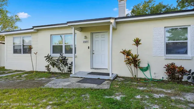 a view of a white house with a big yard and potted plants
