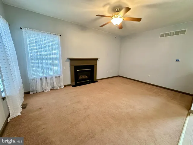 an empty room with chandelier fan and fireplace