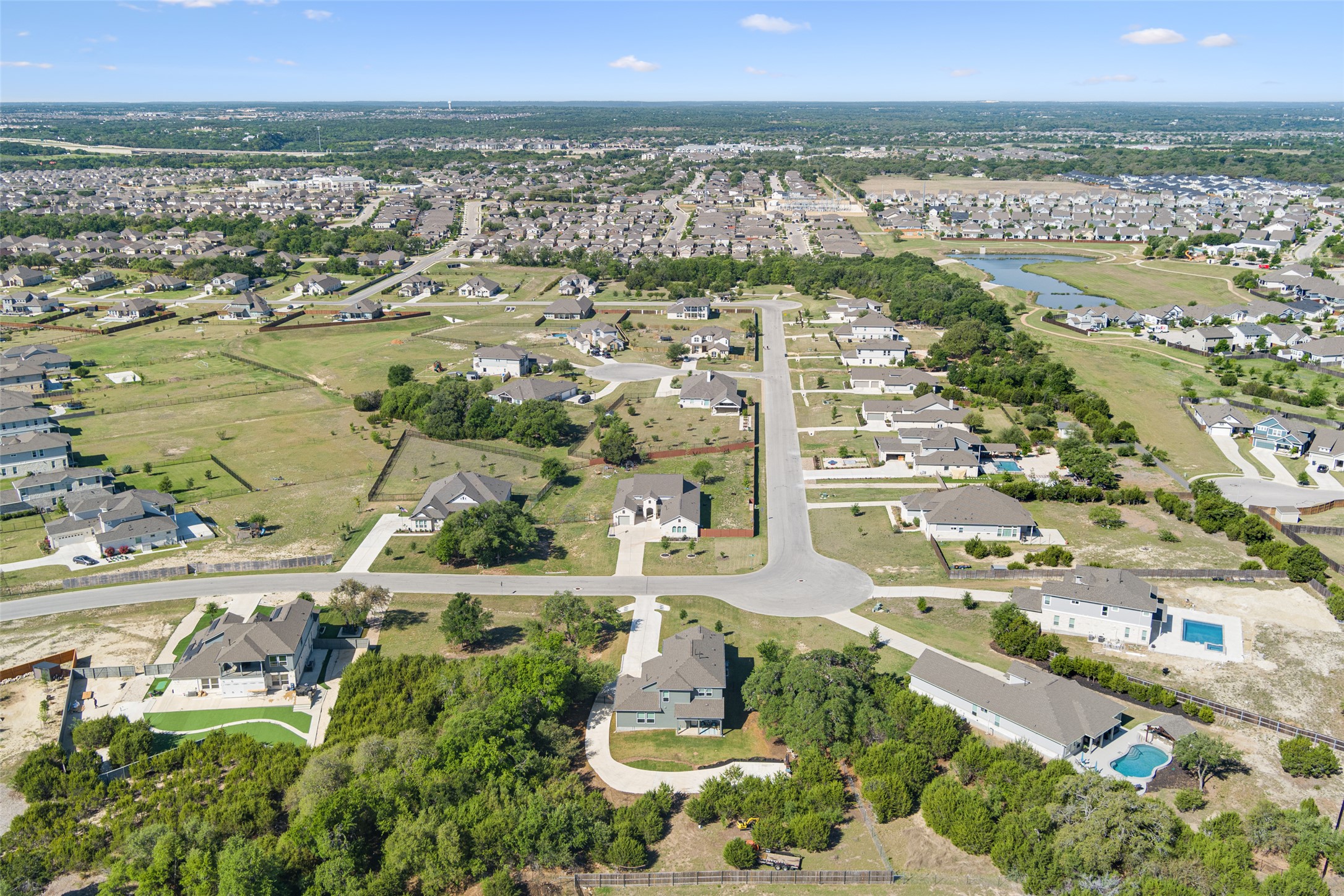 3625 Garrano Bend Leander, TX 78641 - Photo 3 of 38 An aerial perspective reveals a serene residential neighborhood with scattered homes, verdant landscapes, and a tranquil pond, offering a peaceful suburban escape.