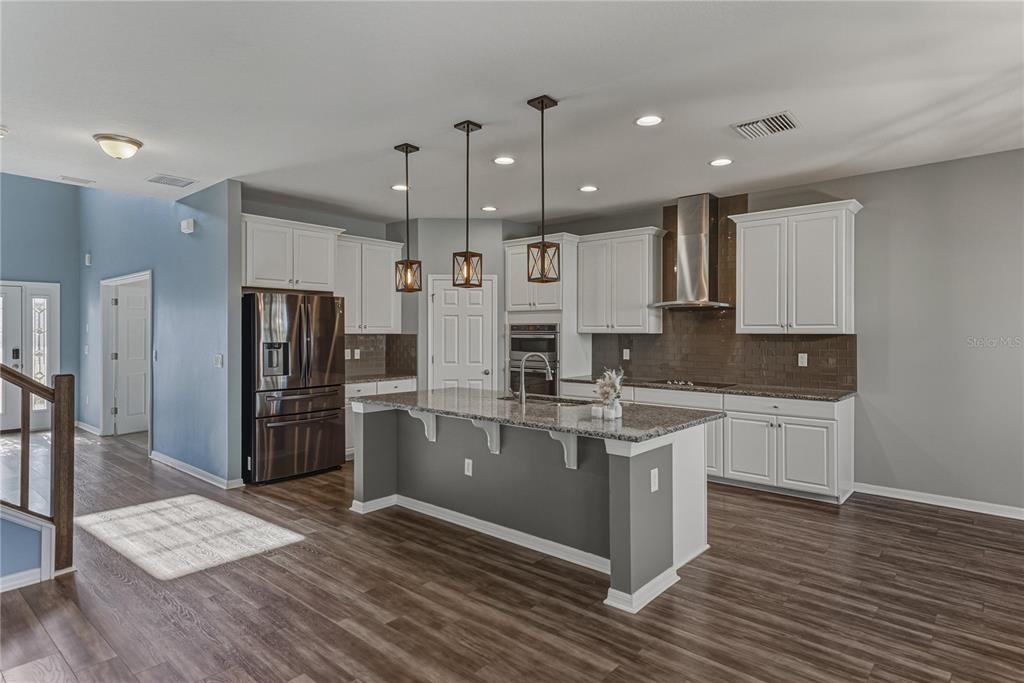 7628 Surf Reed Way Wesley Chapel, FL 33545 - Photo 12 of 76 a kitchen with stainless steel appliances kitchen island granite countertop a refrigerator a stove a sink and white cabinets with wooden floor