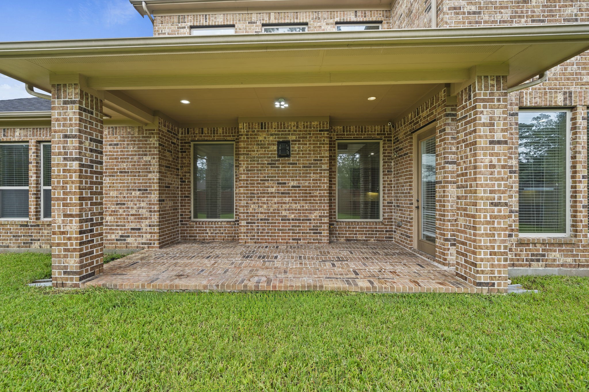 14215 Spindle Arbor Road Cypress, TX 77429 - Photo 40 of 47 This photo showcases a covered brick patio with recessed lighting, surrounded by a well-maintained lawn. The space is ideal for outdoor relaxation and entertaining.