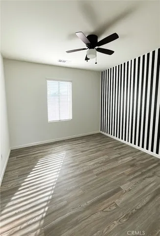 an empty room with wooden floor fan and windows