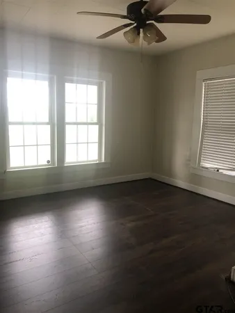 an empty room with wooden floor fan and windows