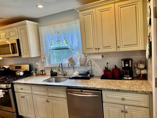 a kitchen with stainless steel appliances granite countertop a refrigerator a stove top oven a sink dishwasher and white cabinets