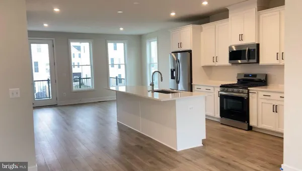 a kitchen with stainless steel appliances kitchen island granite countertop a stove a sink a refrigerator and white cabinets with wooden floor