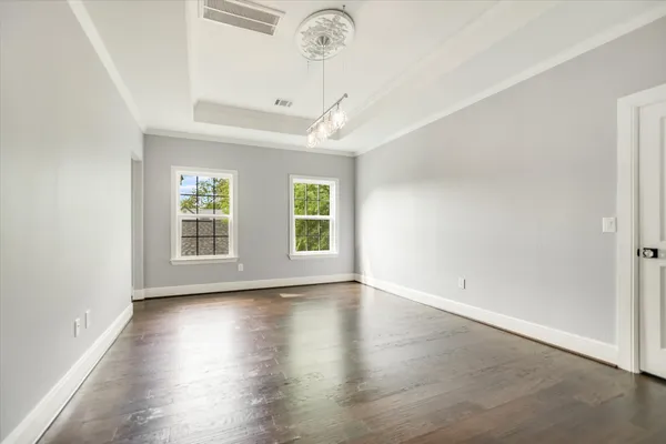 an empty room with wooden floor chandelier and windows