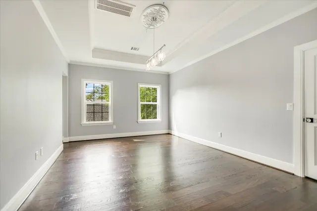 an empty room with wooden floor chandelier and windows