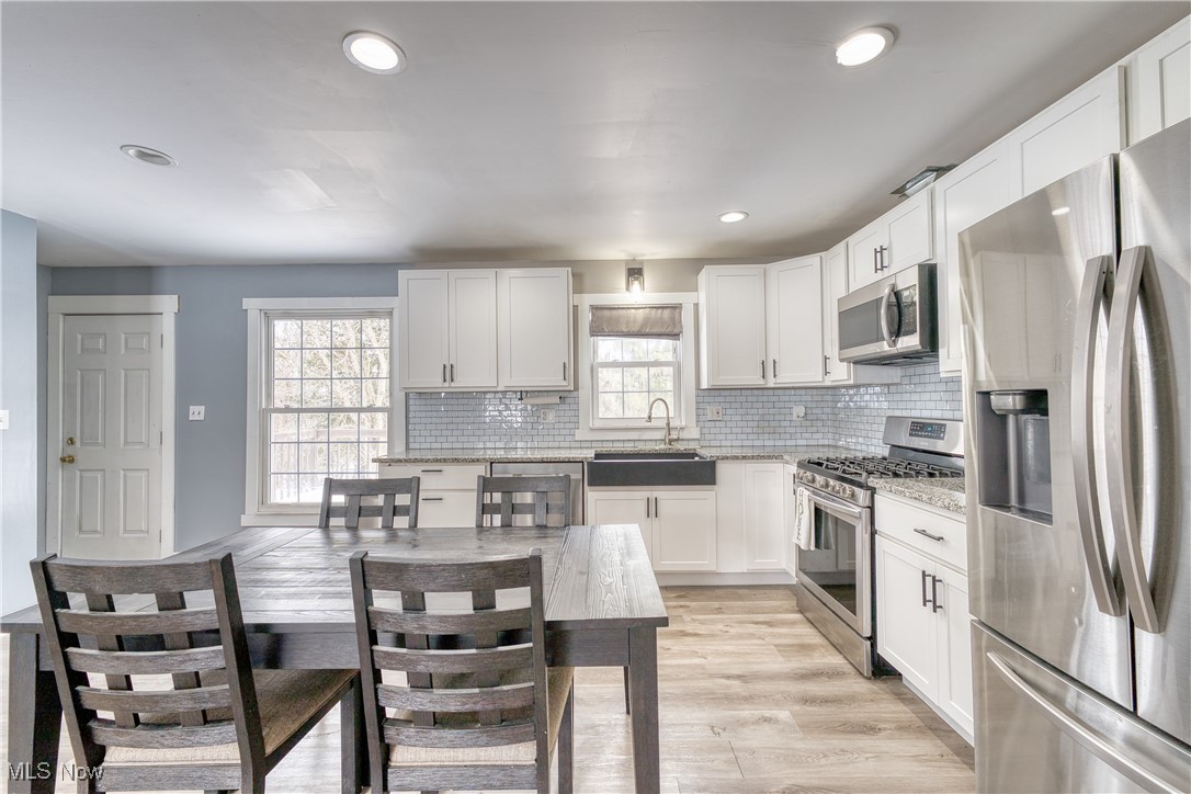 6160 Dresden Road Zanesville, OH 43701 - Photo 13 of 32 Kitchen with appliances with stainless steel finishes, white cabinets, light stone countertops, light wood-style flooring, and decorative backsplash
