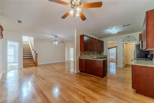 a view of an empty room and kitchen with wooden floor
