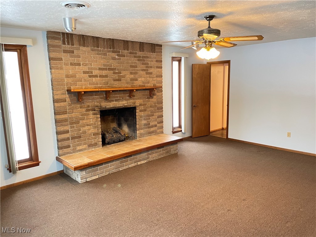1381 Robb Road Conneaut, OH 44030 - Photo 19 of 50 Unfurnished living room with a textured ceiling, carpet flooring, a brick fireplace, and a ceiling fan