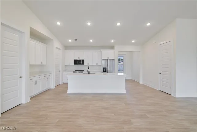 a large white kitchen with kitchen island a sink a center island stainless steel appliances and a counter top space