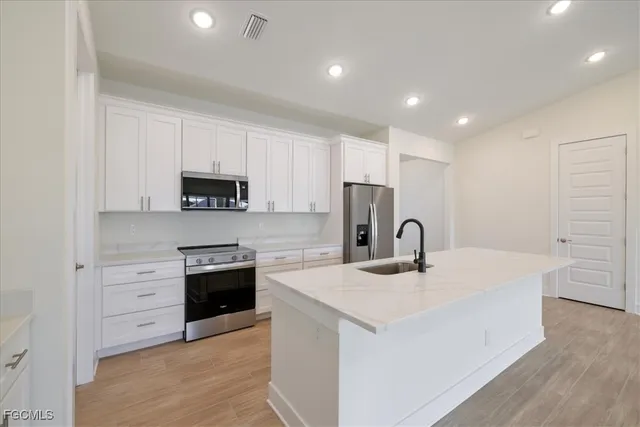 a kitchen with stainless steel appliances granite countertop a kitchen island a stove a sink a refrigerator and white cabinets