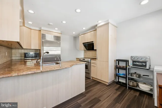 a large kitchen with stainless steel appliances a large counter top space a stove and a wooden floor
