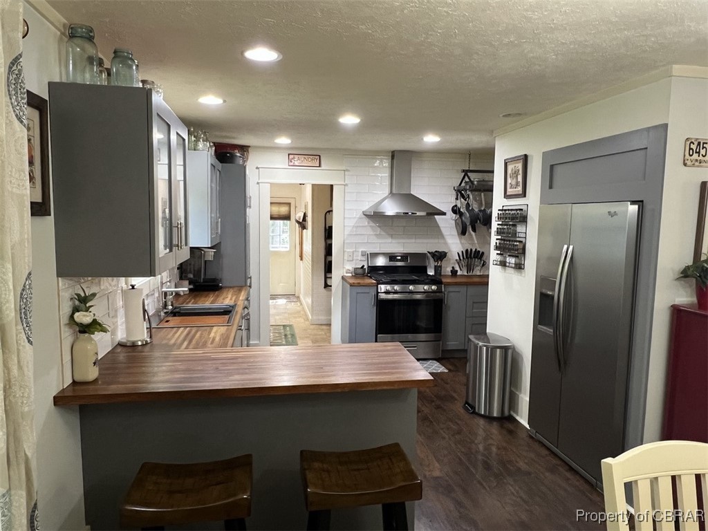 102 Mechams Cove Road Topping, VA 23169 - Photo 21 of 40 Kitchen with wooden counters, stainless steel appliances, backsplash, wall chimney range hood, and gray cabinets