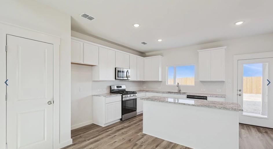 520 Weller Road McKinney, TX 75069 - Photo 2 of 12 Kitchen with stainless steel appliances, a sink, a center island, white cabinetry, and light wood finished floors