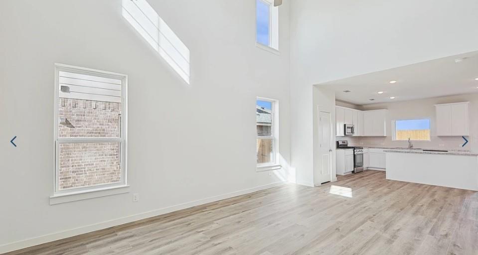 520 Weller Road McKinney, TX 75069 - Photo 9 of 12 Unfurnished living room with a sink, light wood finished floors, a high ceiling, and baseboards