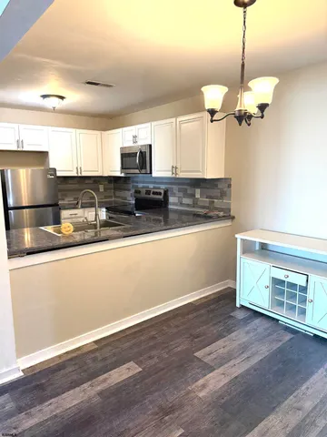 a kitchen with stainless steel appliances granite countertop a refrigerator a sink dishwasher a stove and white cabinets with wooden floor