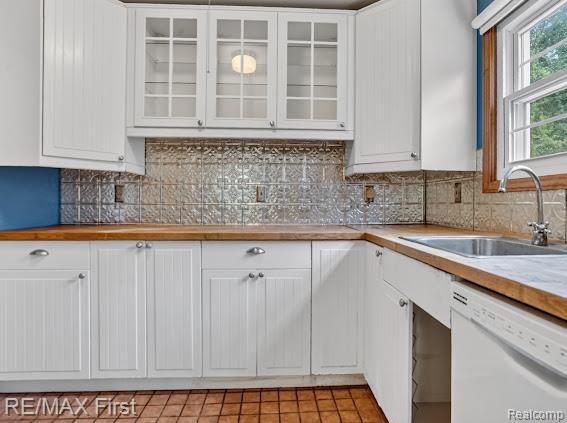 56375 Bates Road New Baltimore, MI 48051 - Photo 20 of 35 Chef's kitchen featuring white shaker cabinetry with glass-front upper cabinets, warm wood-finish countertops, decorative tin tile backsplash, stainless steel sink with chrome faucet, and terra cotta tile flooring