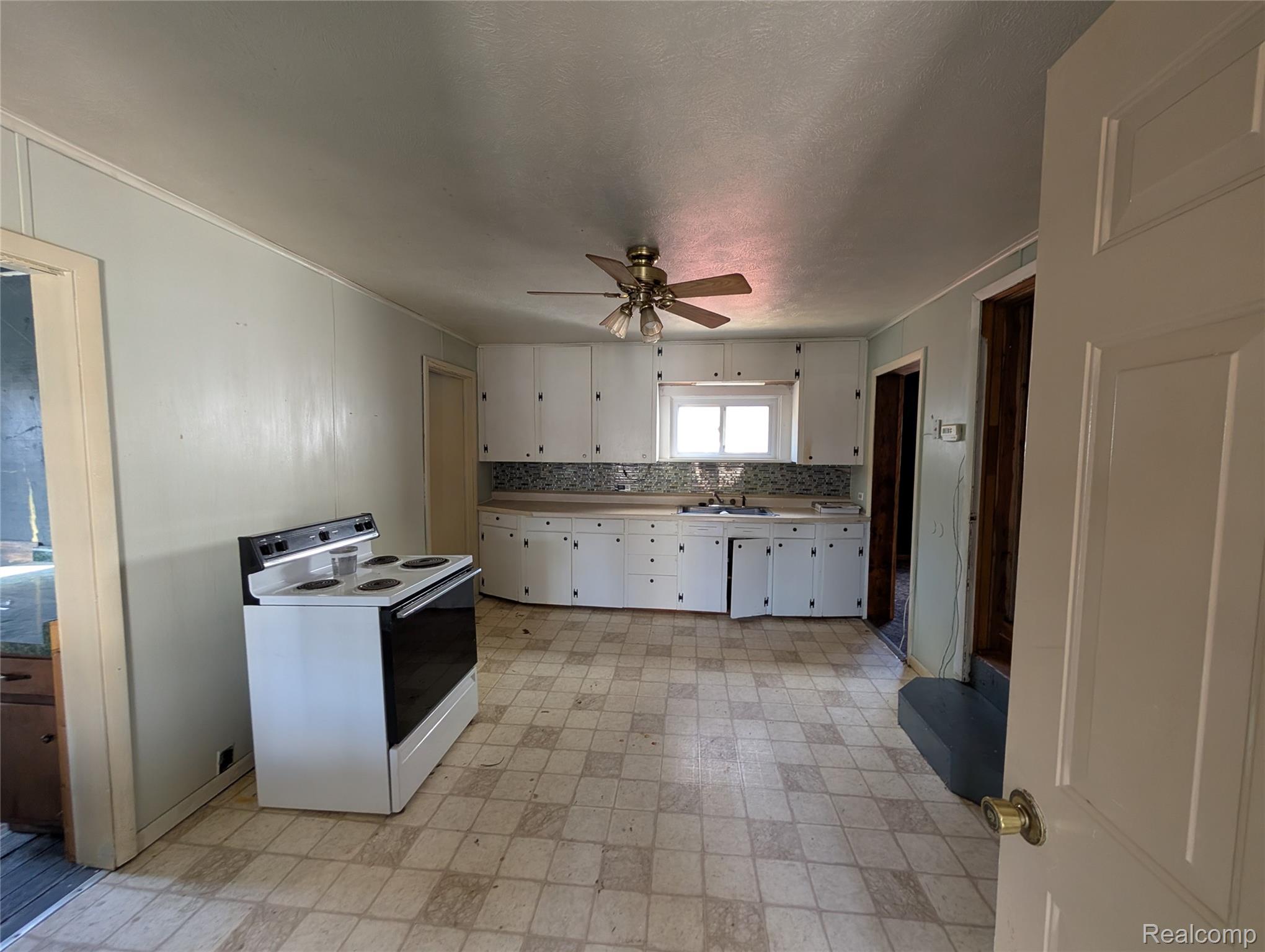 10611 West St Charles Road Sumner, MI 48889 - Photo 3 of 10 Kitchen with white range with electric stovetop, light countertops, light flooring, white cabinets, and tasteful backsplash