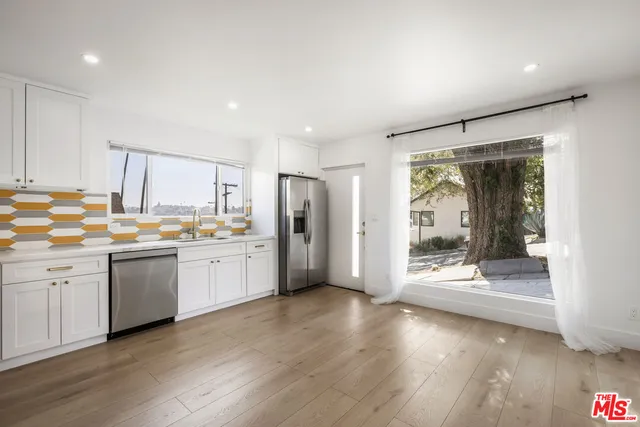 a kitchen with stainless steel appliances granite countertop a refrigerator a sink a stove and white cabinets with wooden floor