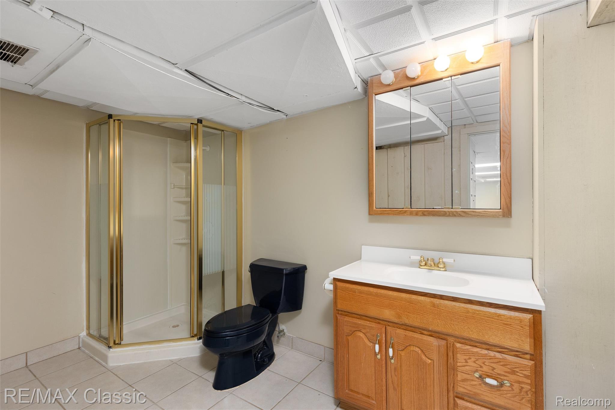 4268 Covered Bridge Road Bloomfield Hills, MI 48302 - Photo 27 of 35 Bathroom featuring a corner shower with a gold-toned frame, a wood-finish vanity with a white countertop, a mirrored medicine cabinet, and a black toilet