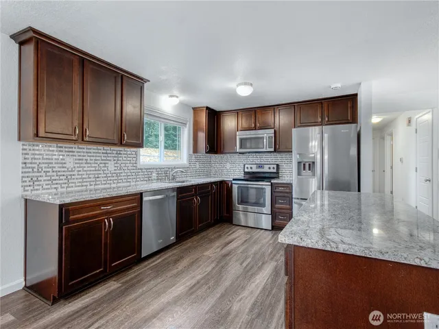 a kitchen with stainless steel appliances granite countertop a stove a sink dishwasher a refrigerator and a oven with wooden floor