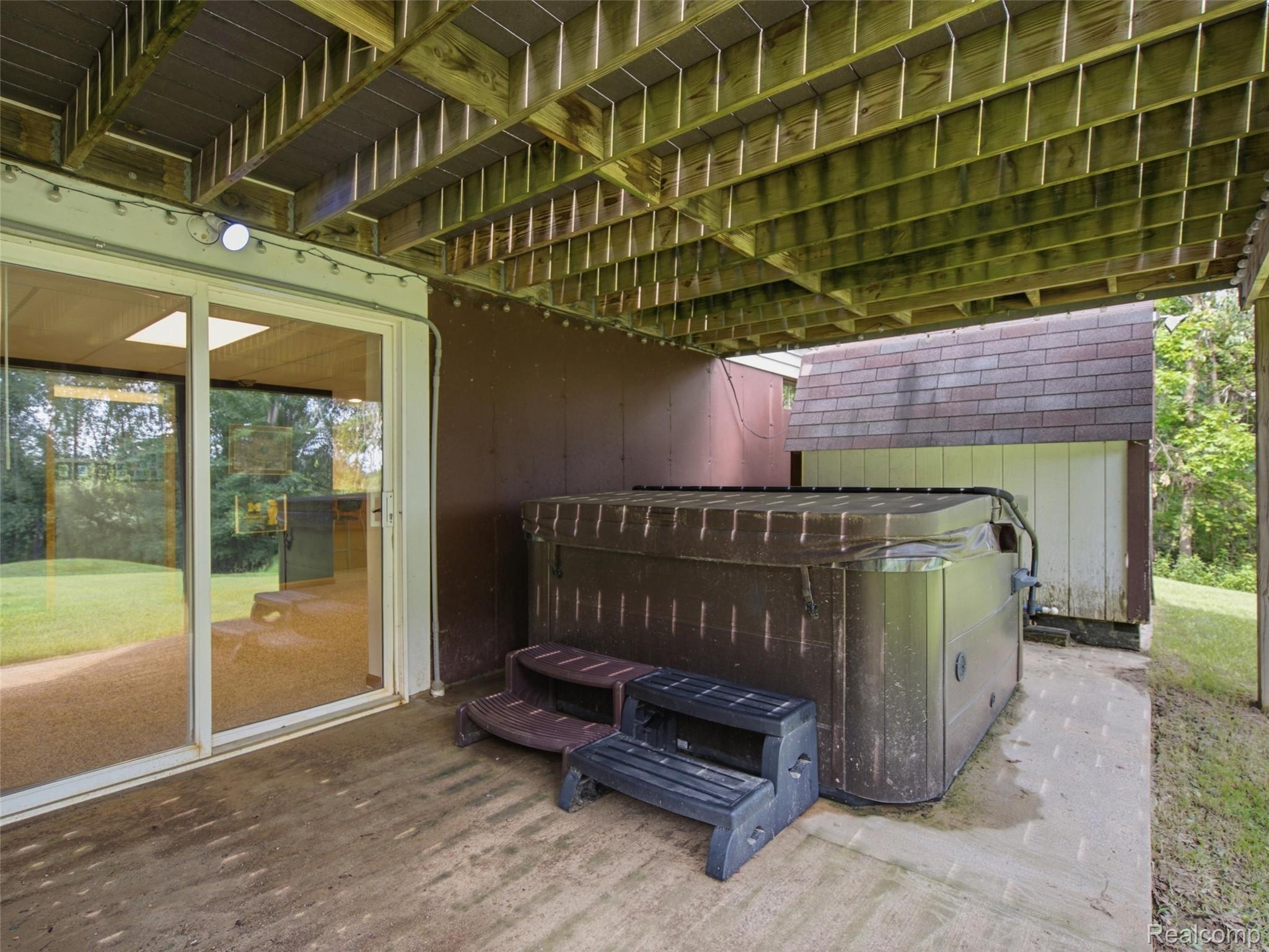 5003 Mason Road Howell, MI 48843 - Photo 40 of 59 Outdoor patio featuring a hot tub with steps, concrete flooring, and an overhead wood-beam deck structure