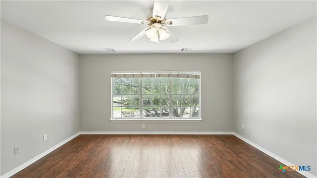 an empty room with wooden floor chandelier fan and windows