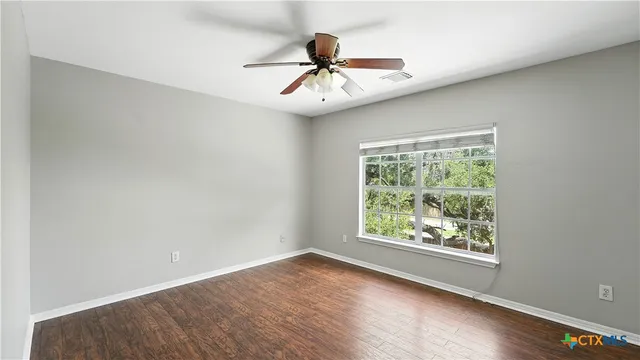 an empty room with wooden floor chandelier fan and windows