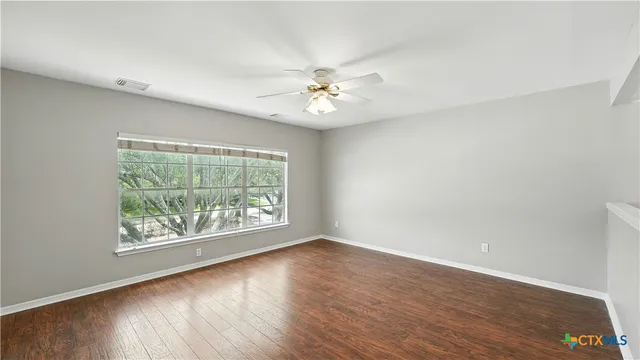 an empty room with wooden floor ceiling fan and windows