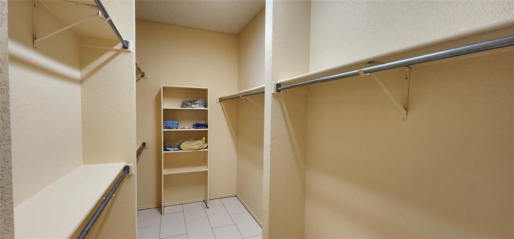 2413 Timber Ridge Lane Flower Mound, TX 75028 - Photo 4 of 16 Walk-in closet with multiple hanging rods, integrated shelving unit, and light-toned tile flooring