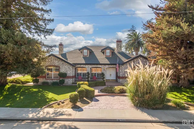 a view of a white house with a fountain plants and large tree