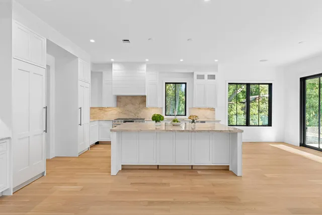 a large white kitchen with granite countertop a stove a sink a refrigerator and white cabinets with wooden floor