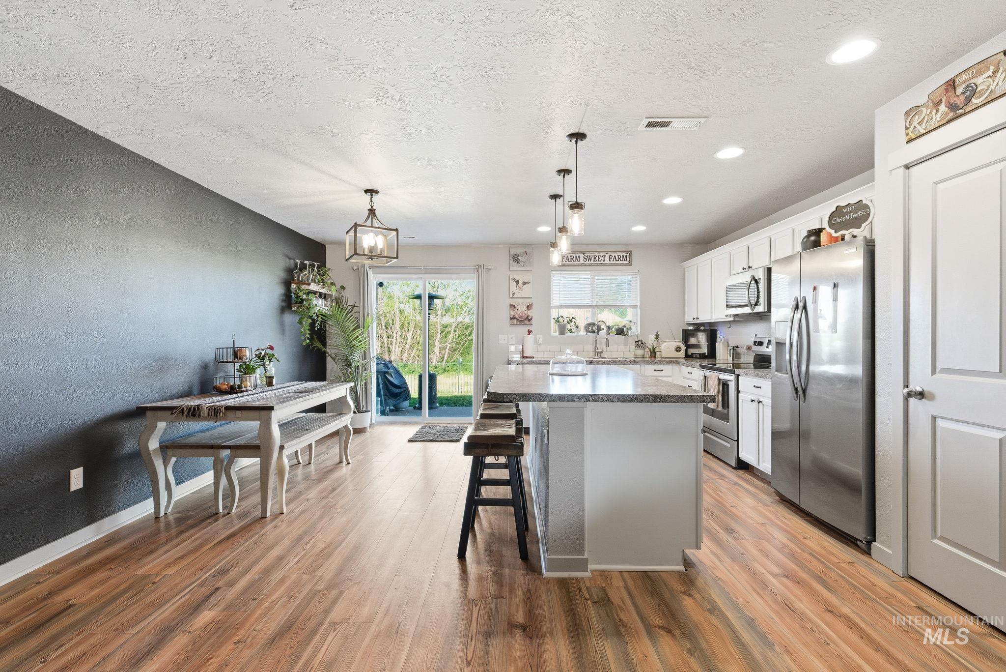 16887 Bethany Avenue Caldwell, ID 83607 - Photo 13 of 50 Open-concept living area featuring wood-finish flooring, a kitchen island with seating, white cabinetry, stainless steel appliances, and a sliding glass door to the exterior