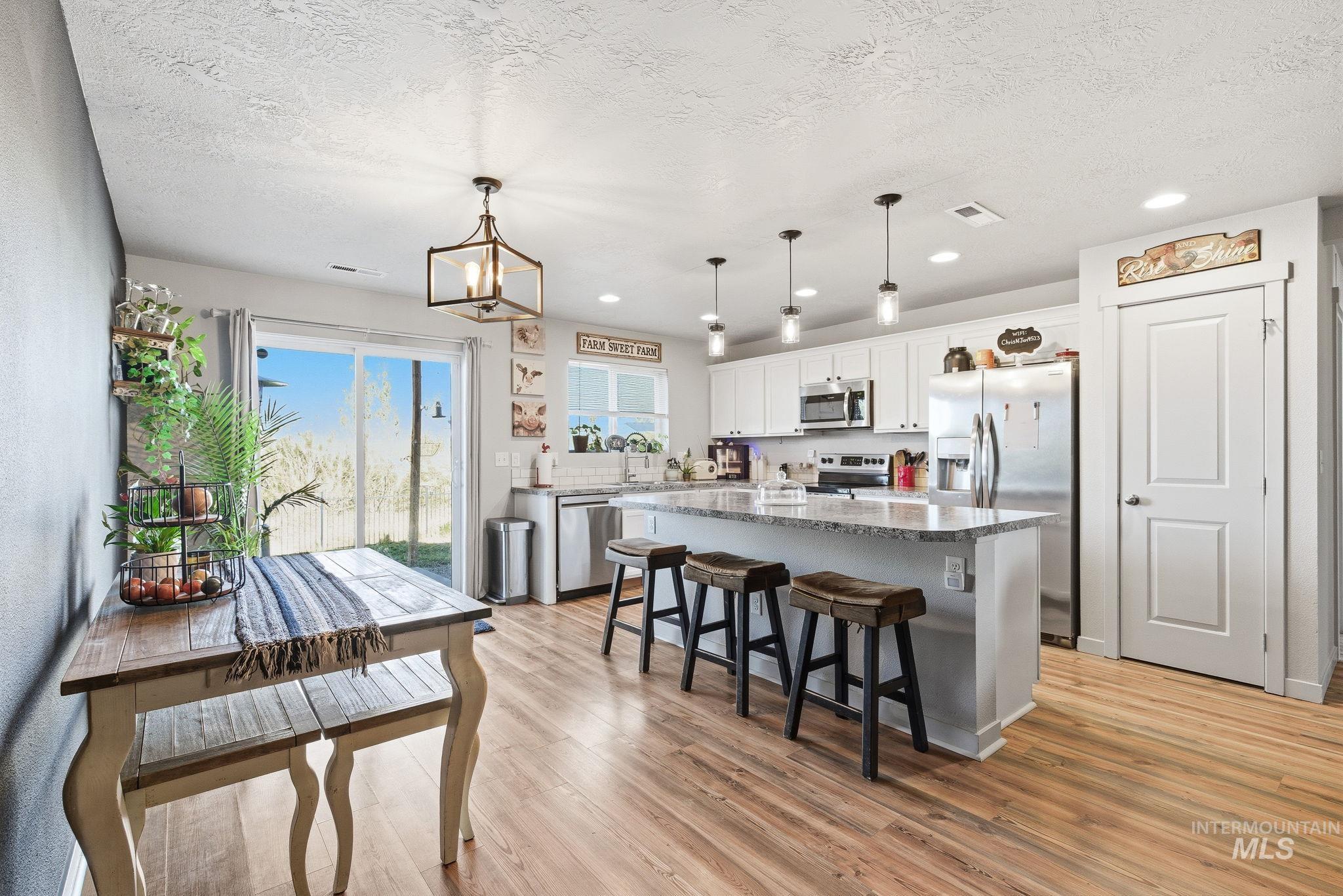 16887 Bethany Avenue Caldwell, ID 83607 - Photo 14 of 50 Open-concept kitchen and dining area featuring wood-finish flooring, white cabinetry, stainless steel appliances, a center island with bar seating, and a sliding glass door