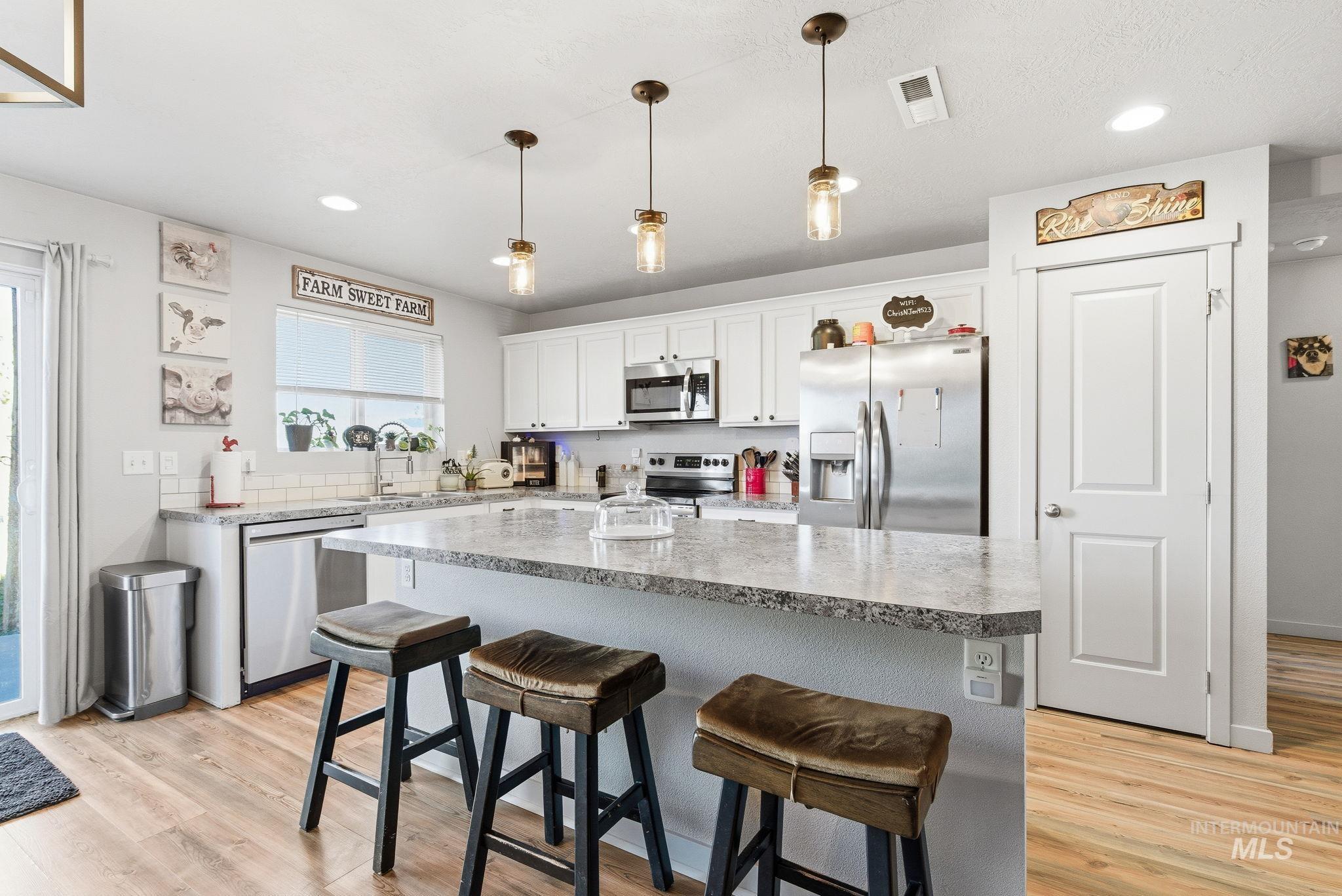 16887 Bethany Avenue Caldwell, ID 83607 - Photo 15 of 50 Kitchen featuring a large island with seating, white shaker-style cabinetry, stainless steel appliances, and wood-finish flooring