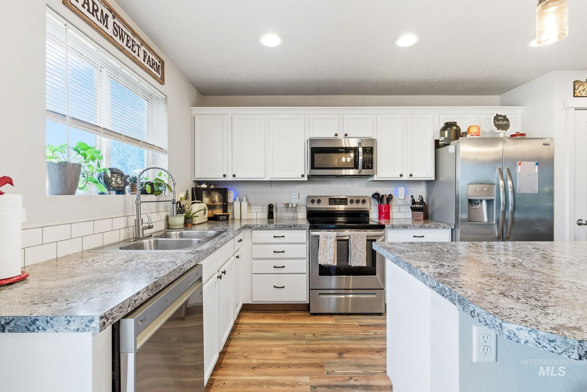 16887 Bethany Avenue Caldwell, ID 83607 - Photo 18 of 50 Modern kitchen featuring white cabinetry, stainless steel appliances, speckled countertops, a subway tile backsplash, and wood-finish flooring
