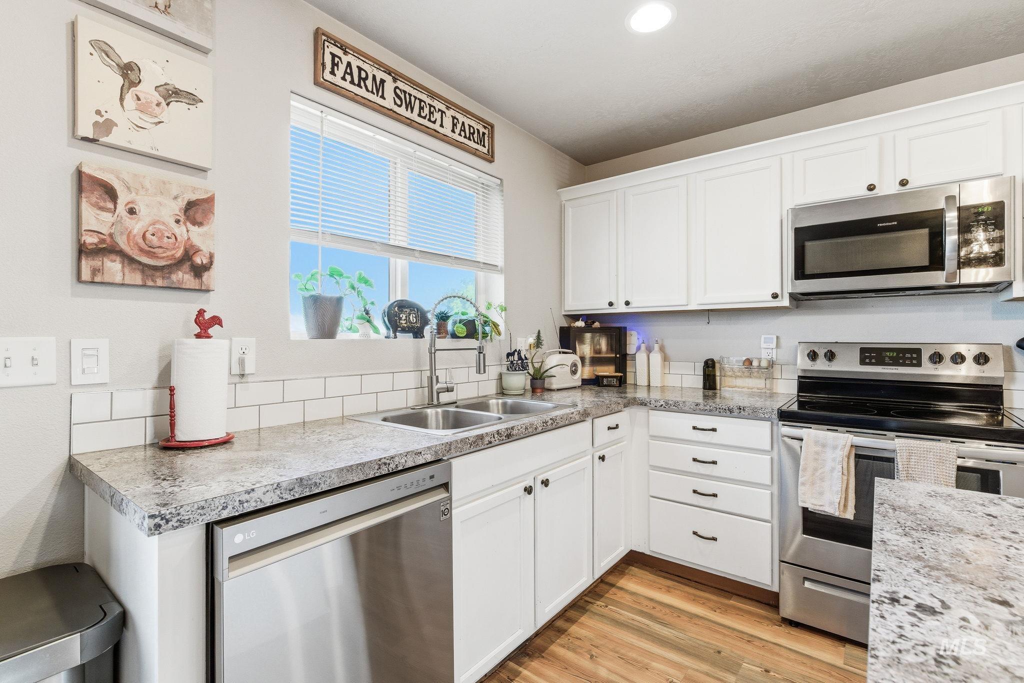 16887 Bethany Avenue Caldwell, ID 83607 - Photo 19 of 50 Kitchen featuring white cabinetry, wood-finish flooring, stainless steel appliances, a double basin sink, and a subway tile backsplash